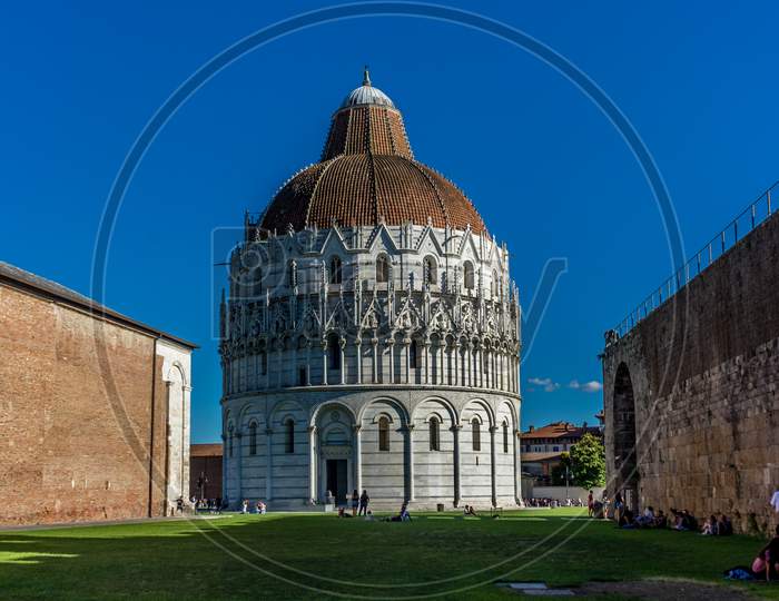 Pisa, Italy - 25 June 2018: Pisa Baptistery Battistero Di Pisa On Piazza Del Miracoli Duomo Square,Camposanto Cemetery, Leaning Tower Of Pisa In Tuscany, Italy