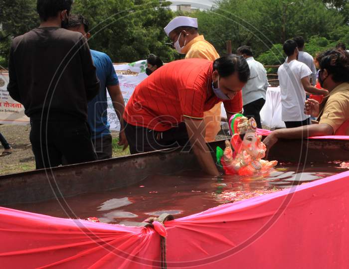 Man Immersing Idol Of Lord Ganesha In A Community Tank