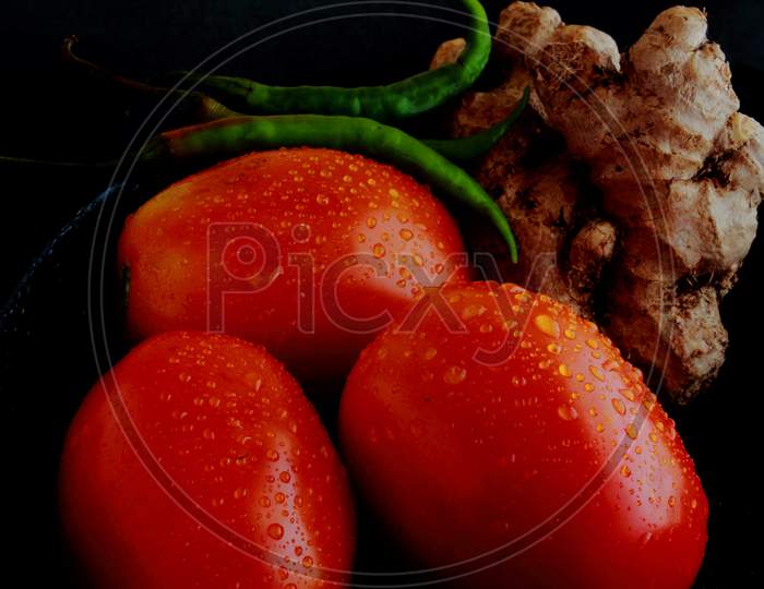 Tometos, green chillies and ginger root on black background