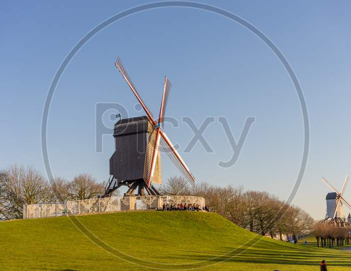 Belgium, Bruges, Windmill Island, A Group Of People Flying Kites In A Field With Windmill Island In The Background