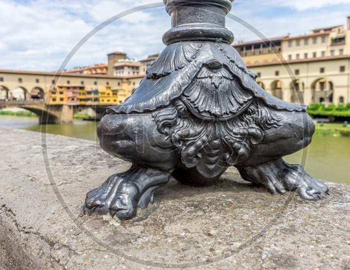 The Base Of The Lamp Post Near Ponte Vecchio Over The Arno River In Florence, Italy