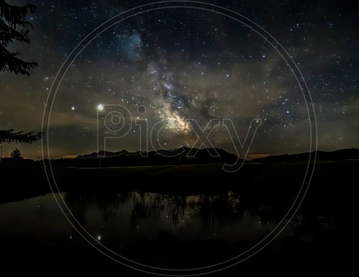 A starry night with thee Milky Way partly reflecting in a little pond at the so called Winklmoosalm in the Mountains of Reit im Winkl in Bavaria, Germany.