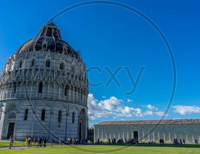 Pisa, Italy - 25 June 2018: Pisa Baptistery Battistero Di Pisa On Piazza Del Miracoli Duomo Square,Camposanto Cemetery, Leaning Tower Of Pisa In Tuscany, Italy