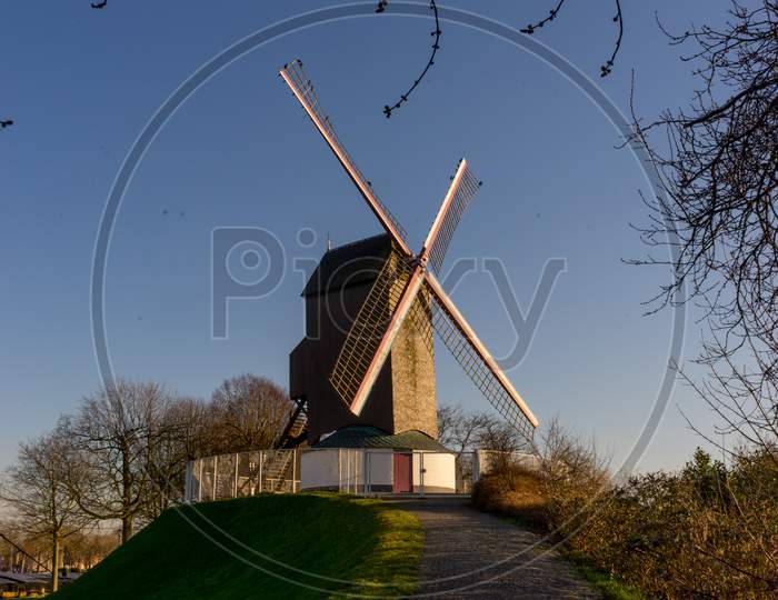 Belgium, Bruges, Bonne Chiere, A Close Up Of A Lush Green Field With Path Leading To Windmill Sunset