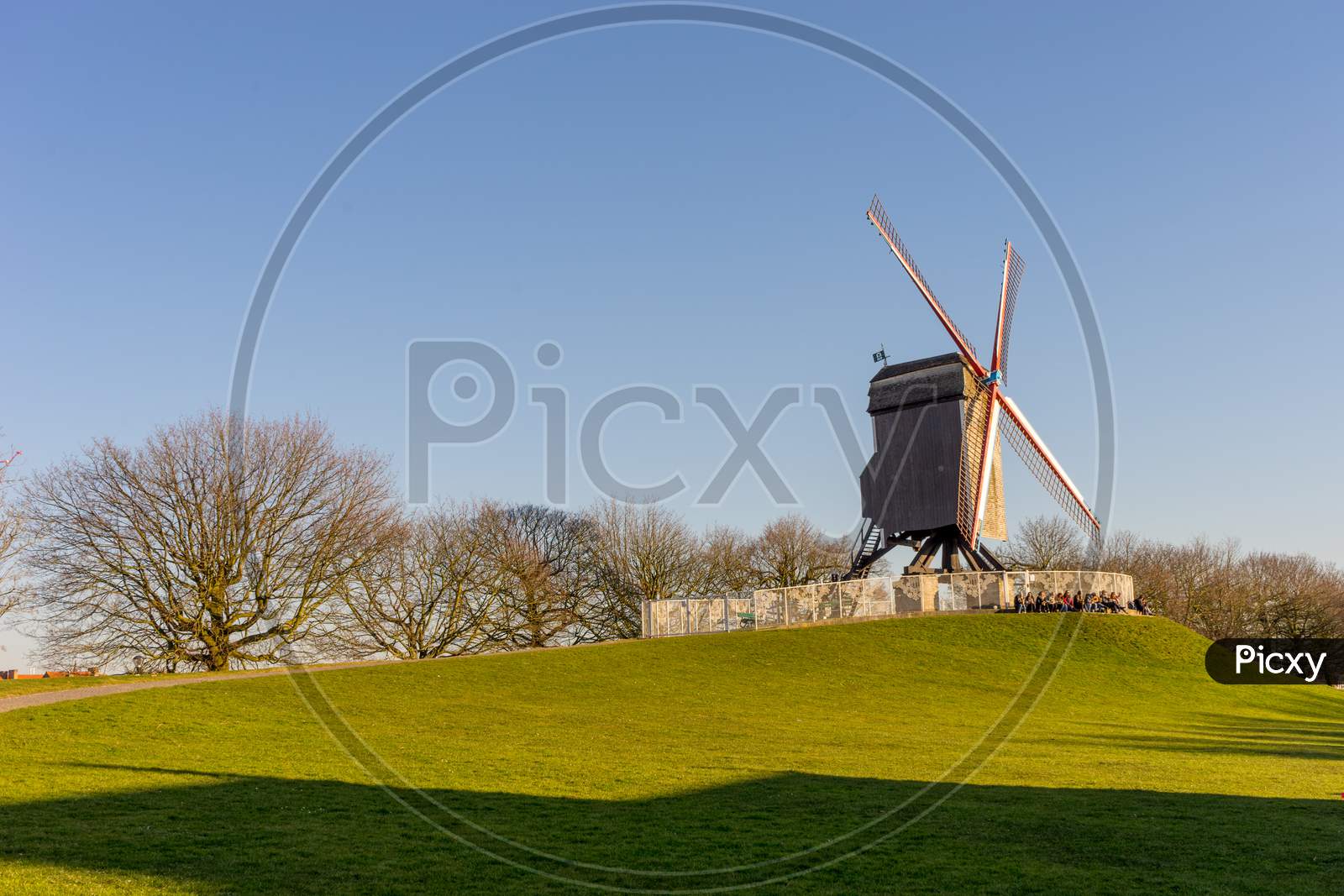 Belgium, Bruges, Windmill Island, A Group Of People Flying Kites In A Field With Windmill Island In The Background