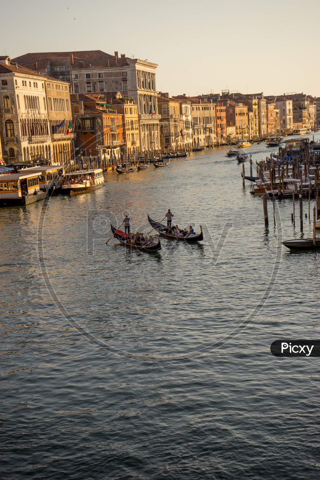 Gondolier Taking Tourists On A Gondola Ride Along The Grand Canal Near Rialto Hotel In Venice, Italy