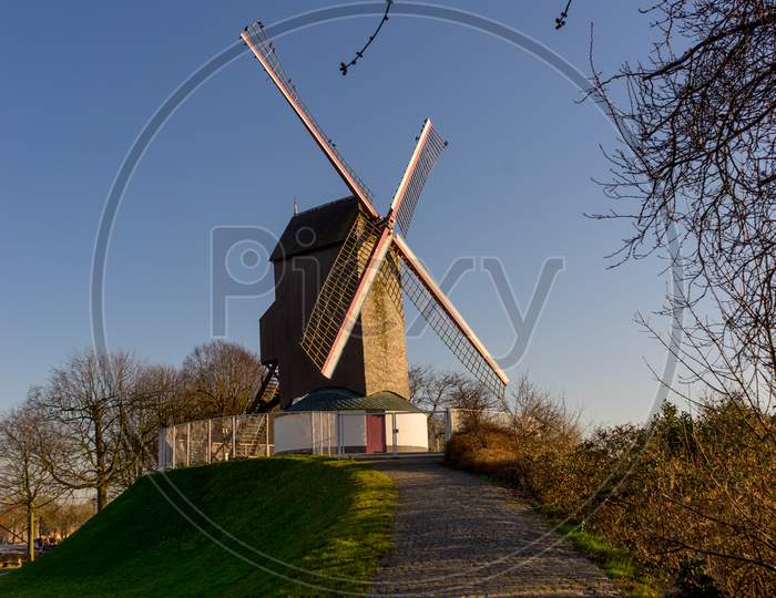 Belgium, Bruges, Bonne Chiere, A Close Up Of A Lush Green Field With Path Leading To Windmill Sunset