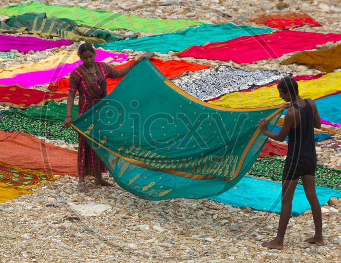 A Close up view of a Washerman and women rinsing a Indian Saree before placing on the pebbles for drying under the Sunlight by the side of a river near Mysuru in Karnataka/India.