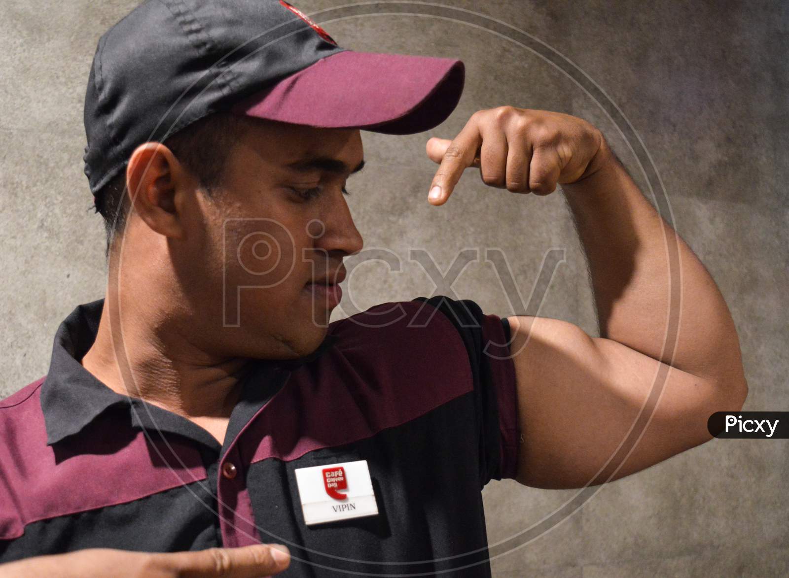 A Cafe Staff Showoff His Bicep In Cafe Uniform At Cafe Indoor.