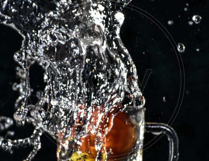 Splash Of Red Tomato And Yellow Lemon Dive Into Glass Of Water With Black Background