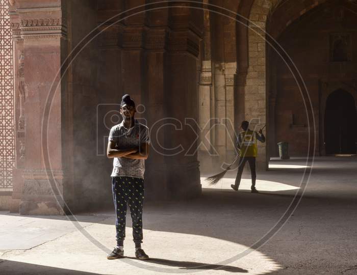 A Indian Boy Giving Pose For Fashion Shoot Inside Of Old Fort And Asi Employee Cleaning The Area.