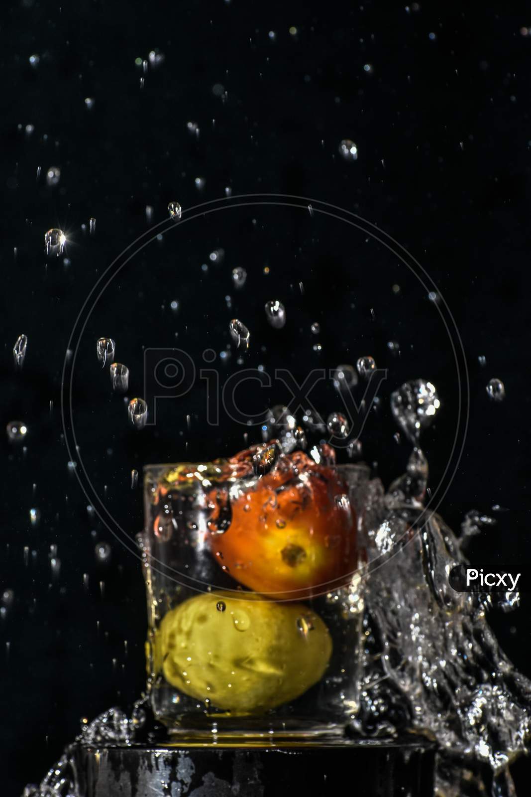 Splash Of Red Tomato And Yellow Lemon Dive Into Glass Of Water With Black Background