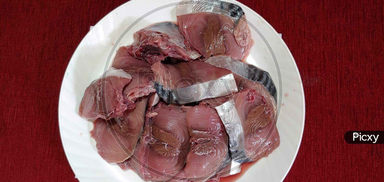 SLICED FRESH RAW TUNA FISH PREPARED FOR COOKING, ISOLATED ON A WHITE PLATE