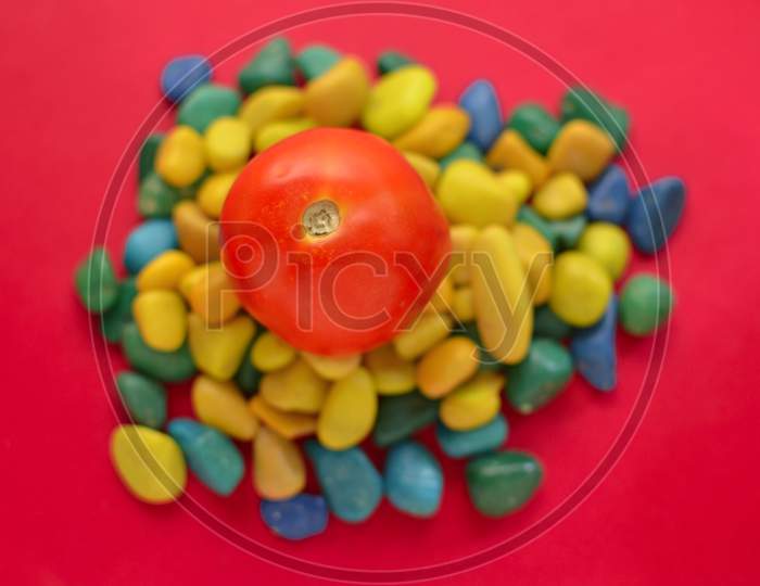 Red Tomato Kept On Multicolor Pebbles And On Red Background