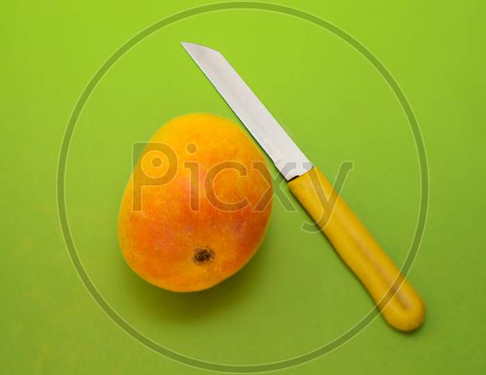 A Yellow Indian Alphanso Mango And Knife On Green Background