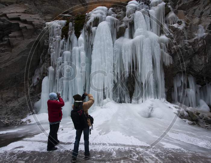 Photographers In Red and yellow Jackets In Front Of A High Altitude Frozen Water Falls In Leh In India