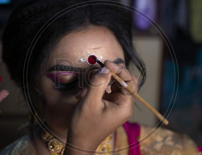 A Makeup Artist Drawing A Beautiful Design Called Kolka Or Bindi In India On The Forehead Of A Bride