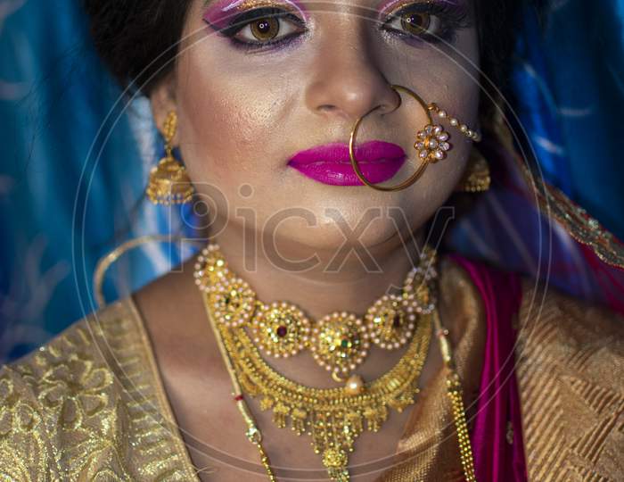 Portrait Of A Cute Indian Model In Bridal Look With Heavy Gold Jewelry And Red Sari