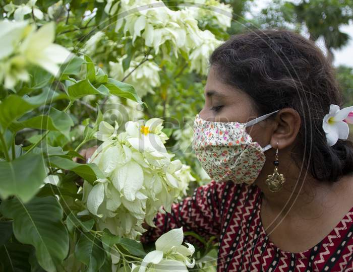 Beautiful woman wearing floral designer mask smells flowers