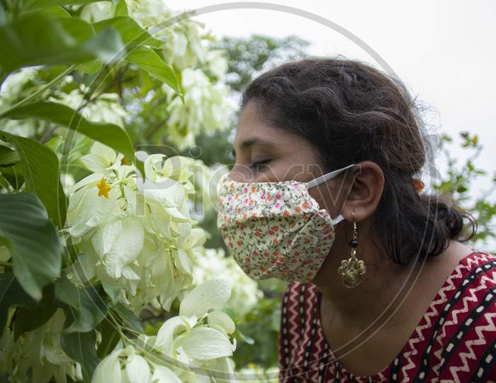 Beautiful woman wearing floral designer mask smells flowers