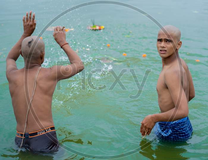A hindu devotee splashing water in powai after offering pooja another devotee staring at camera