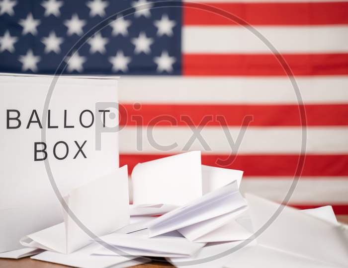 Ballot Box With Votes On Table Before Counting With Us Flag As Background Concept Of Ballot Or Vote Counting After Us Election