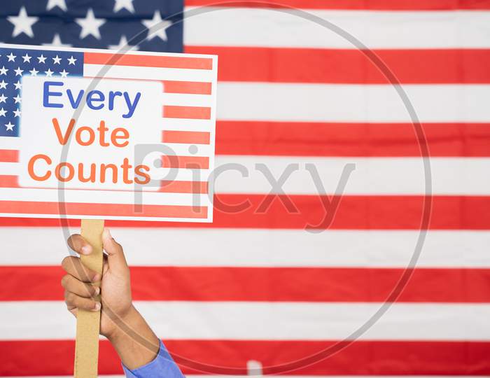 Hands Holding Every Vote Counts Sign Board With Us Flag As Background With Copy Space - Concept Of Voter Rights And Us Election.