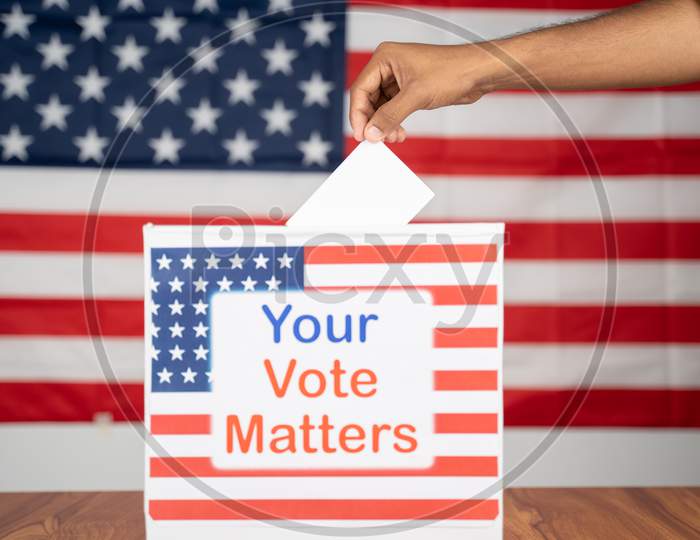 Close Up Of Hands Placing Vote Inside The Ballot Box With Your Vote Matters Printed With Us Flag As Background - Concept Of Voter Rights And Us Election.