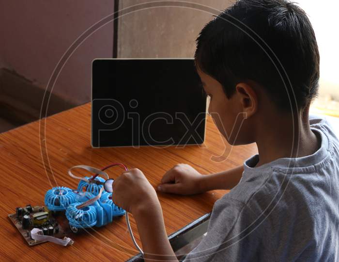 An 8 year old child is learning to make drone in online coding class with black screen tab. electric Soldering iron in kids' hand. closeup image.  concept kids coding classes.