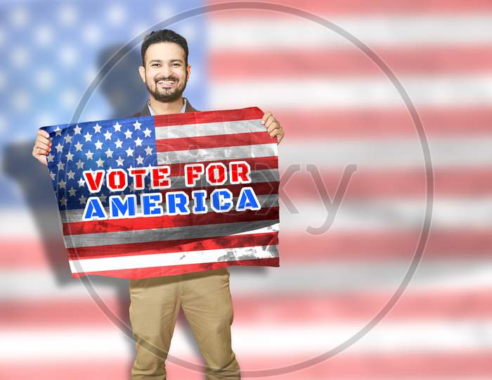 Presidential Election 2020 Concept, Cheerful Young Man Holding American Flag With I Vote Ameraica Text On It, Copy Space. Usa Politics.