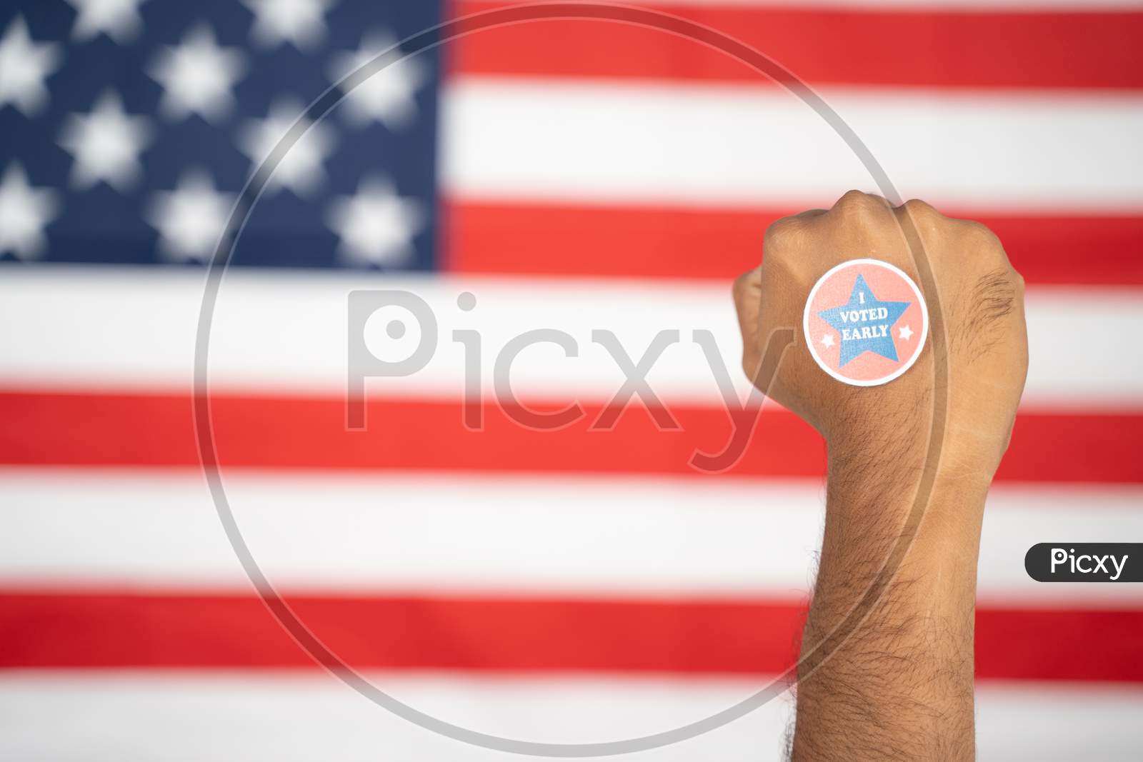 Rising Fist With I Voted Early Sticker On Hand With Us Flag As Background - Concept Of Early Voting At Us Election.