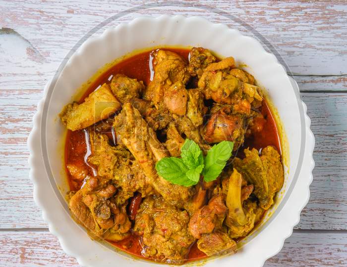 Chicken curry or masala , spicy reddish chicken leg piece dish garnished with coriander leaf and arranged in a white ceramic bowl with wooden background