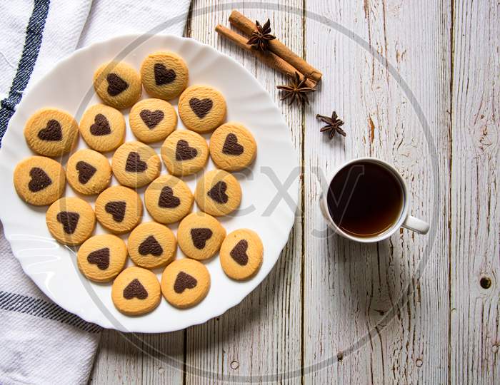 Top view of chocolate chip heart shaped cookies and cinnamon sticks and cup of coffee