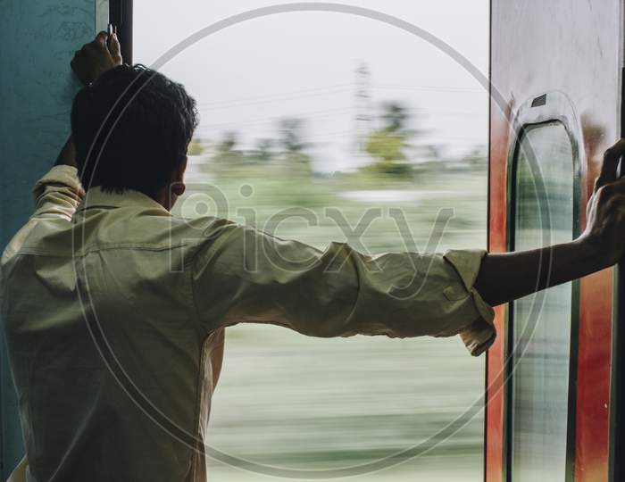 Man looking out of a moving train door into greenery