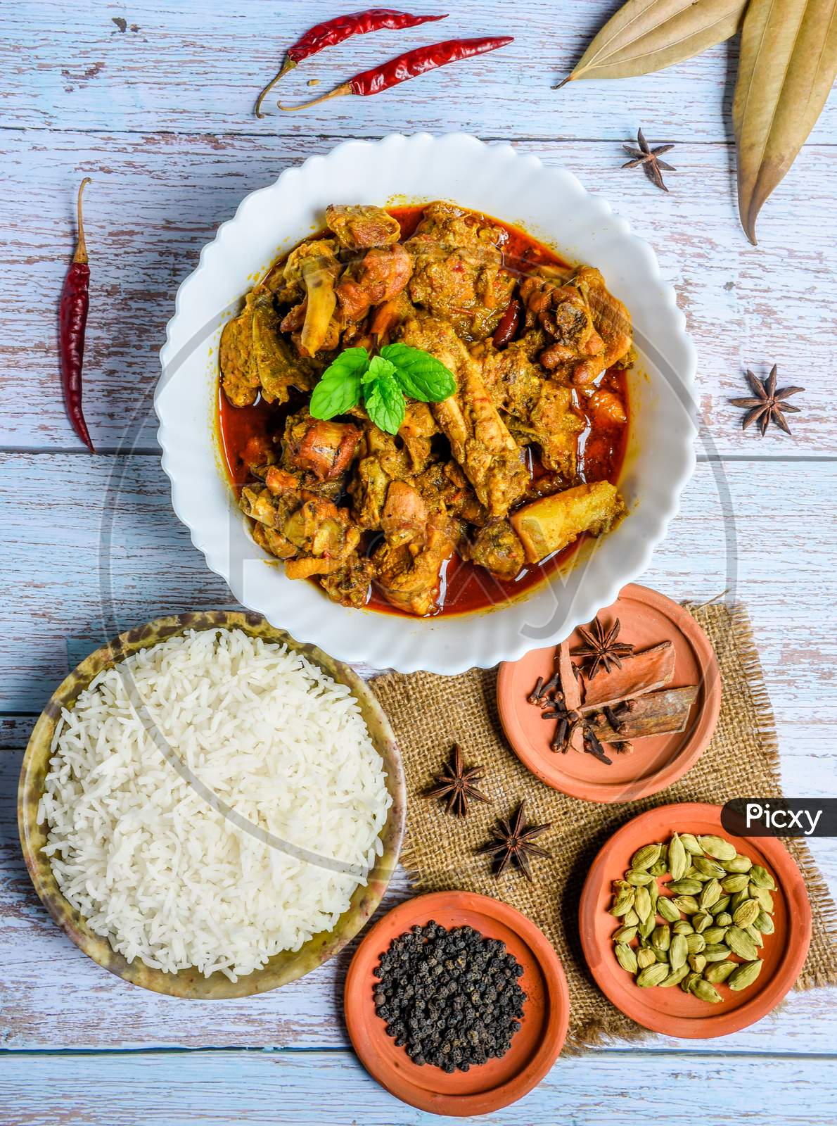 Chicken curry or masala , spicy reddish chicken leg piece dish garnished with coriander leaf and arranged in a white ceramic bowl with wooden background