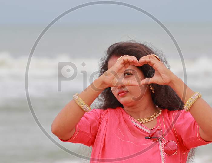 A South Indian Female Model Posing On The Marina Coast Of Chennai With The Help Of Fingers Of Both Hands Composing The Heart