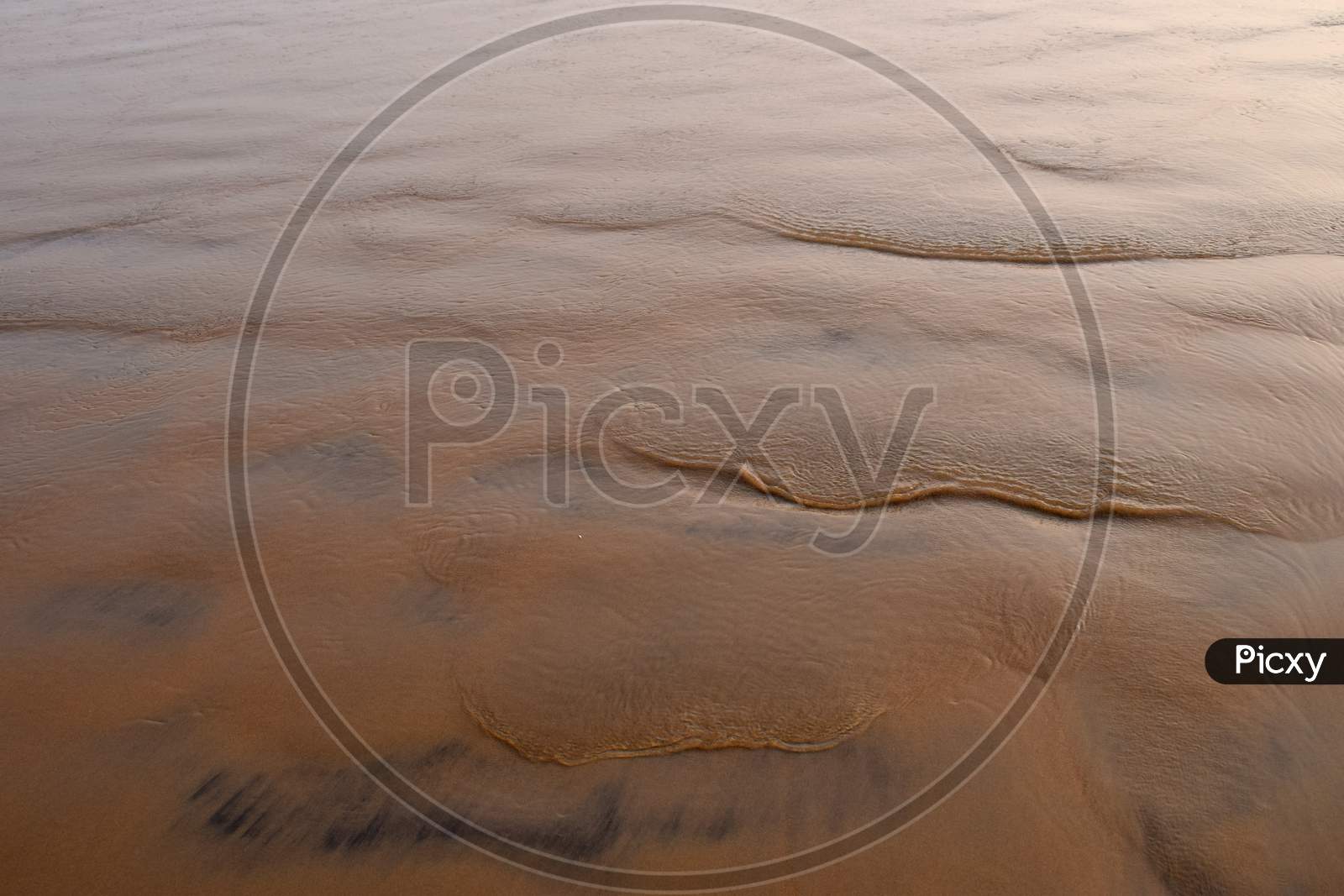 Waves Pattern On Sand Beach. Close Up To Sand Texture With Wave Marks On The Beach