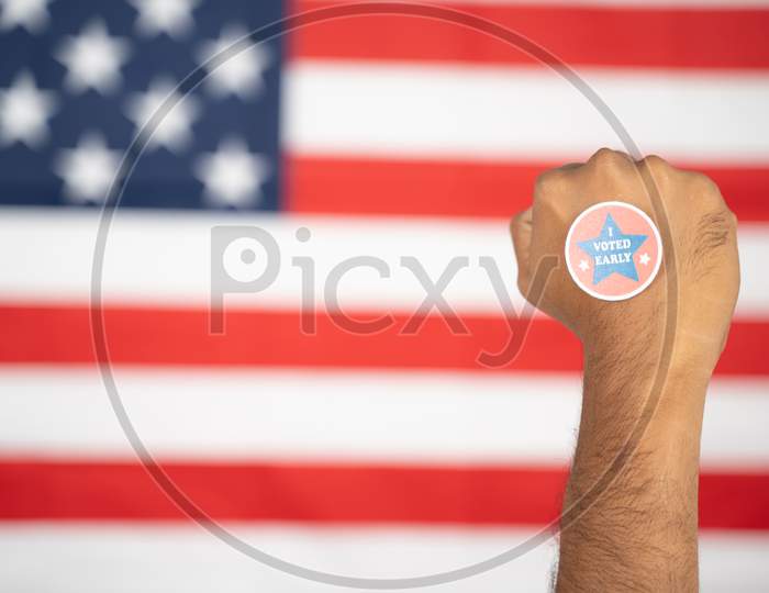 Rising Fist With I Voted Early Sticker On Hand With Us Flag As Background - Concept Of Early Voting At Us Election.