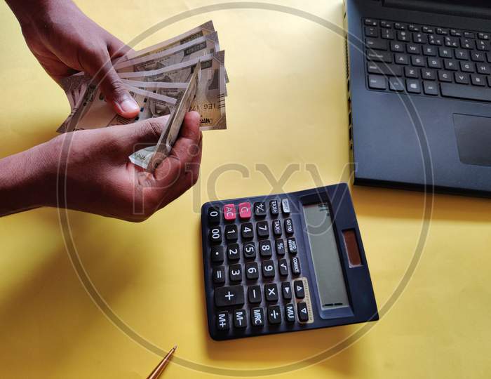 South Indian Man Counting Money. Calculating Bills Using Calculator,Laptop. Yellow Background