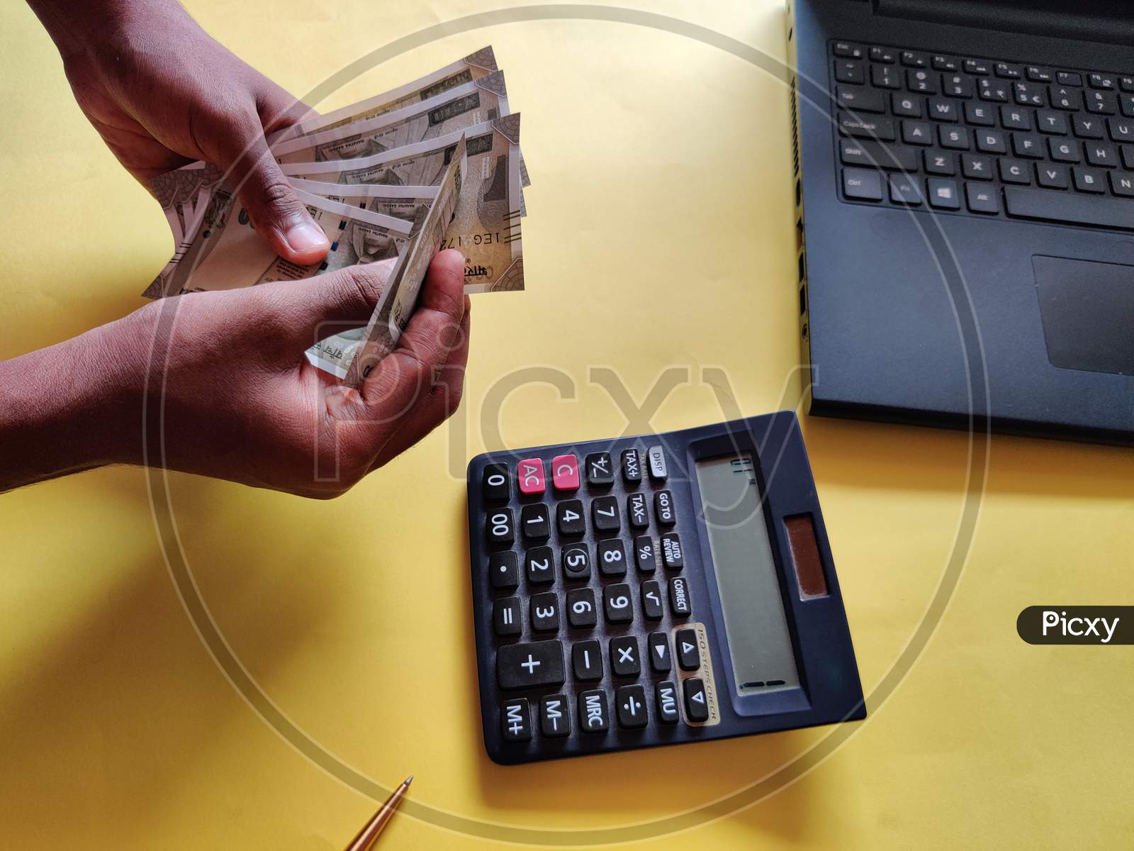 South Indian Man Counting Money. Calculating Bills Using Calculator,Laptop. Yellow Background