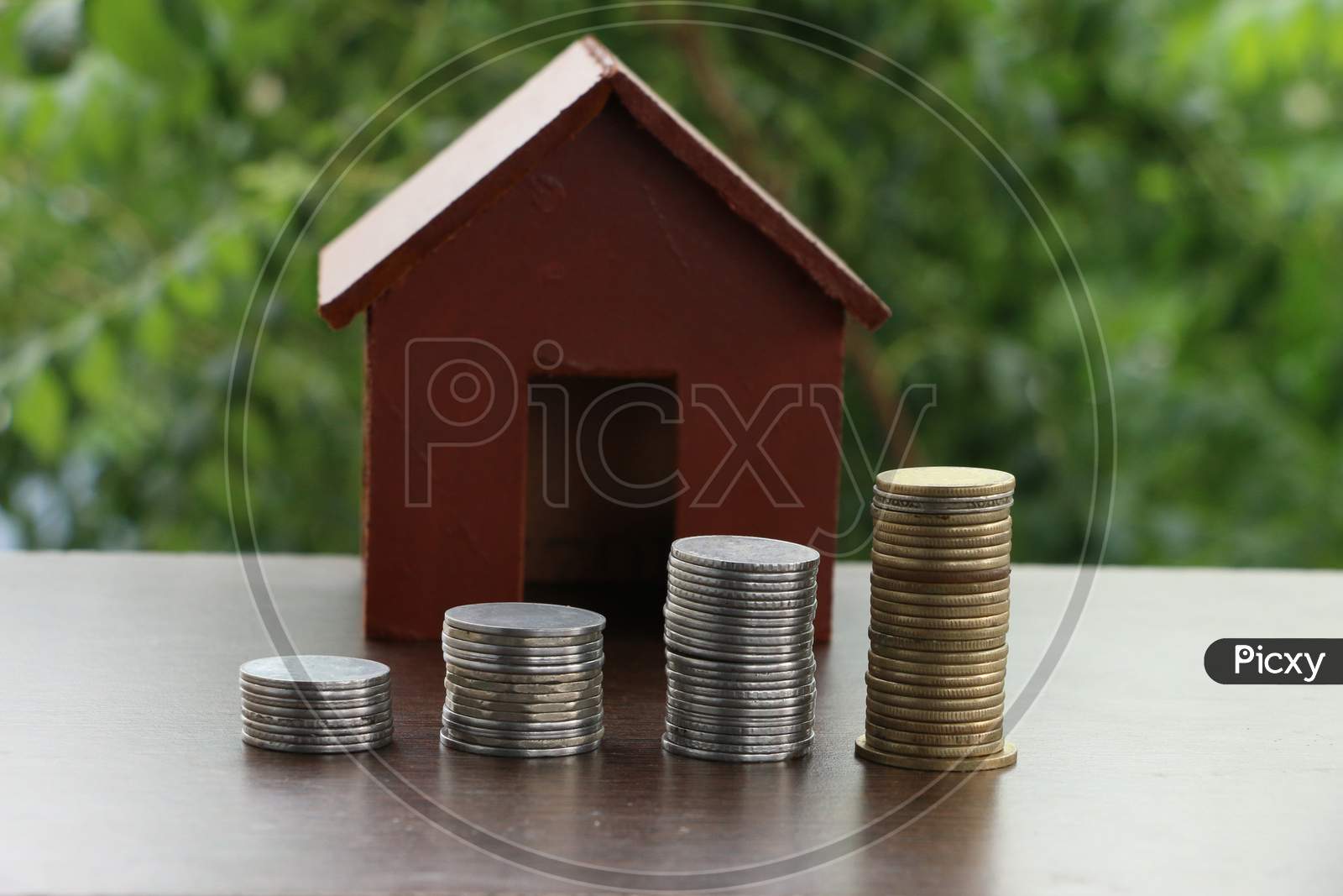 Money Coin Stack Growing Graph With Home Model On Wood Table In The Public Park Background. Saving Money And Investment Concept.