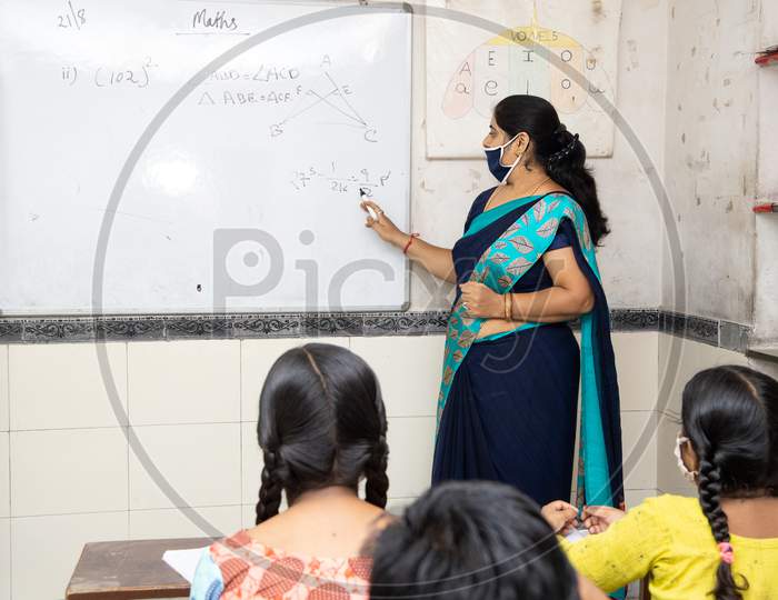 Indian Teacher And Students Wearing Face Masks Maintaining Social Distancing Study In Classroom Back At School During Covid19 Pandemic.