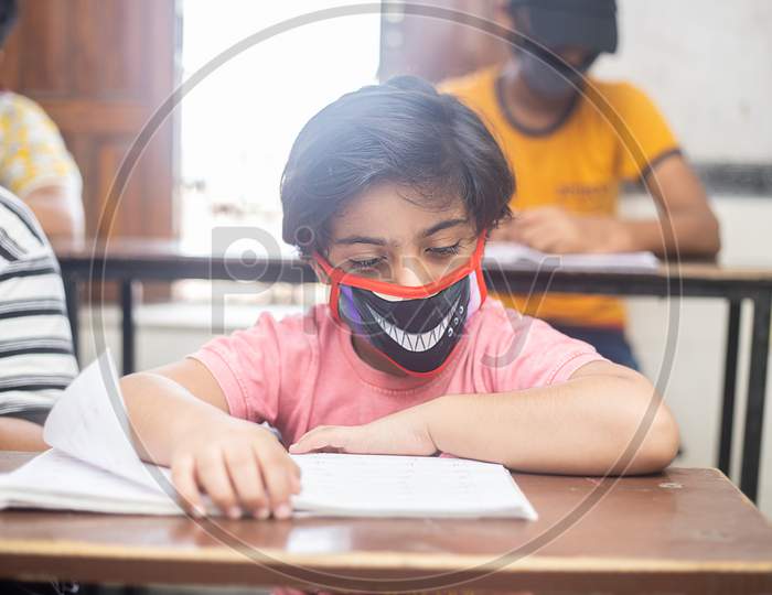 Indian Boys Students Studying In Classroom Wearing Mask Maintaining Social Distancing Looks At Camera, School Reopen During Covid19 Pandemic, New Normal. Selective Focus