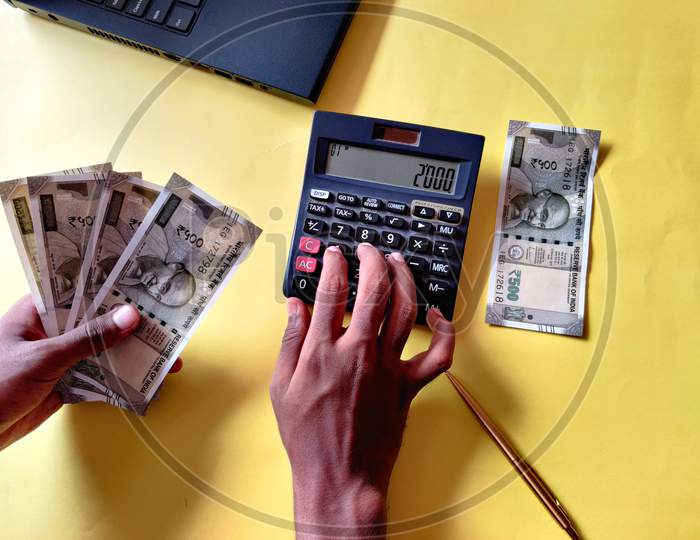 South Indian Man Five Hundred Rupees Notes. Calculating Bills Using Calculator,Laptop. Yellow Background