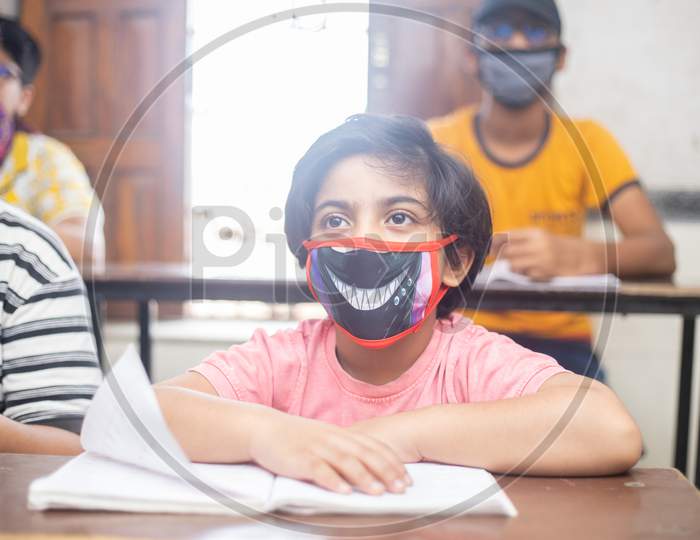 Indian Boys Students Studying In Classroom Wearing Mask Maintaining Social Distancing Looks At Camera, School Reopen During Covid19 Pandemic, New Normal. Selective Focus