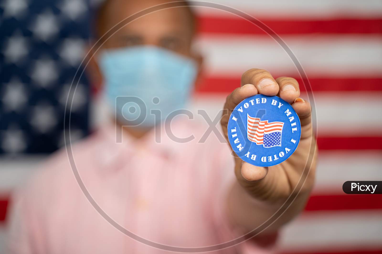 Man In Medical Mask Showing I Voted By Mail Sticker With Us Flag As Background - Concept Of Mail In Voting At Usa Election.