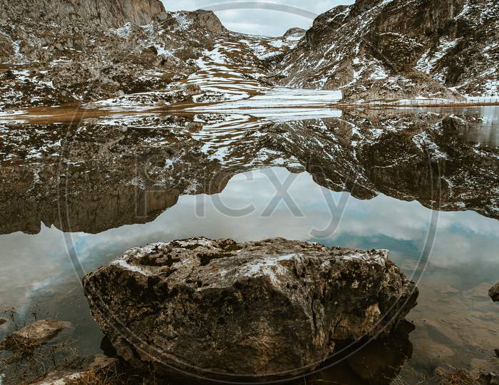 Close Up Of A Rock Inside A Frozen Lake In Front Of A Giant Mountain During Winter