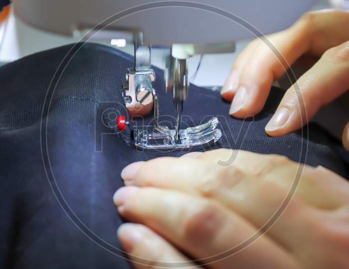 Sewing Concept. Female Hands Working At A Modern Sewing Machine With Some Fabrics And Textiles