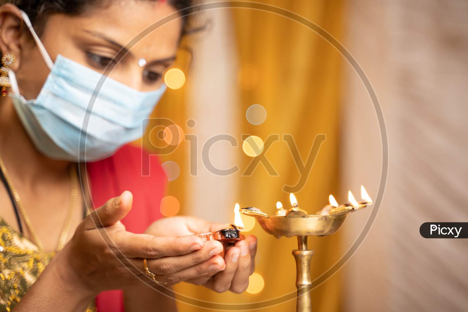 Selective Focus On Hands, Indian Woman In Medical Mask Lighting Lantern Or Diya Lamp During Festival At Home - Concept Of Traditional Festival Celebrations During Coronavirus Or Covid-19 Pandemic