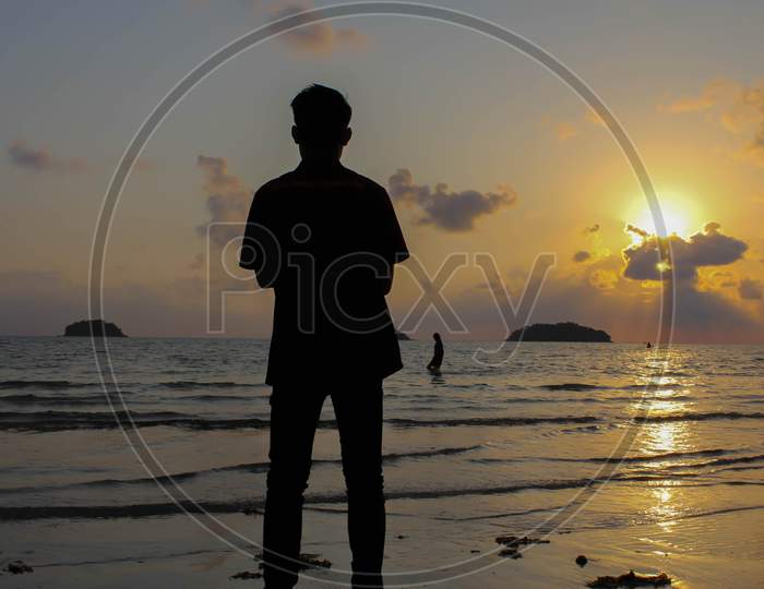 Lonely Man Stands On The Beach Looks Towards The Sun Light